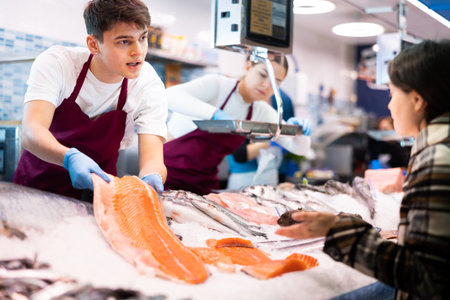 Responsive salesman demonstrating piece of salmon in fish store