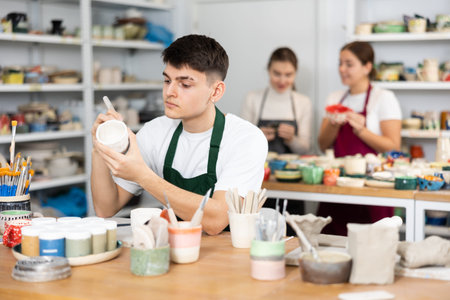 Young man painting pottery in workshopの写真素材