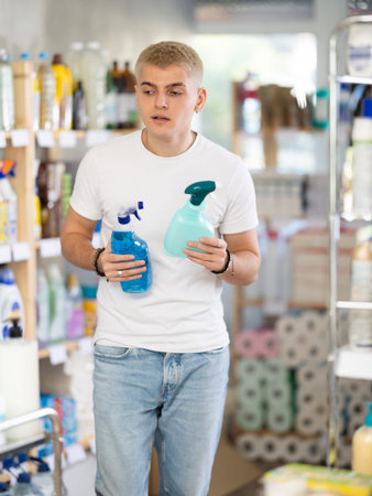 Attentive young guy choosing between two sprays standing between shelves in supermarketの写真素材