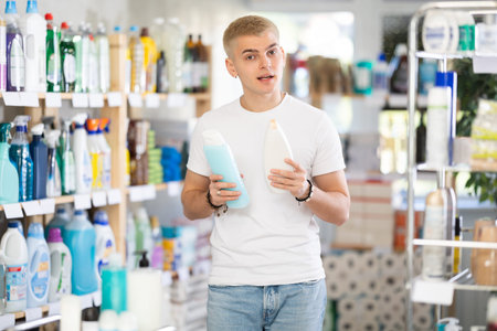 Guy buyer chooses shampoo or shower gel in household goods department of supermarketの写真素材