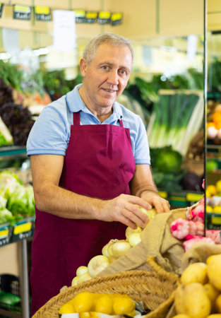 Professional old male seller putting onion on shelves in grocery shopの写真素材