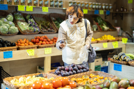 Young woman chooses plums in storeの写真素材
