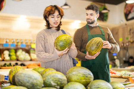 Young male seller offering melon to girl in grocery marketの写真素材
