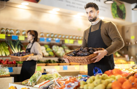 Male employees in uniform carries a wicker basket with avocado in grocery shopの写真素材