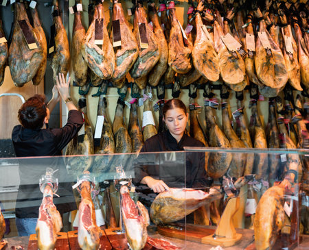 Young couple work together in butcher shop - they cut traditional Spanish jamonの写真素材