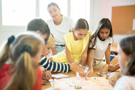 Schoolkids playing board game with teacher in classroomの写真素材