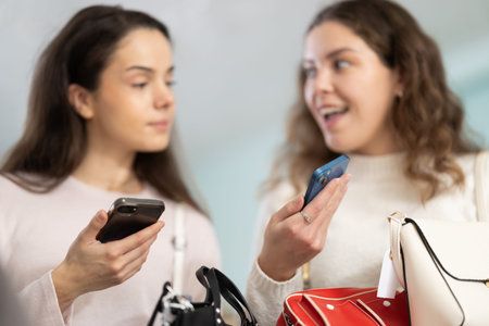 Two girls interesting goods, scans QR code and label of handbagの写真素材