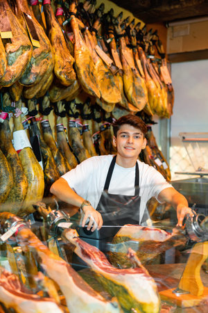 Positive young man carving jamon slices from pigs legの写真素材
