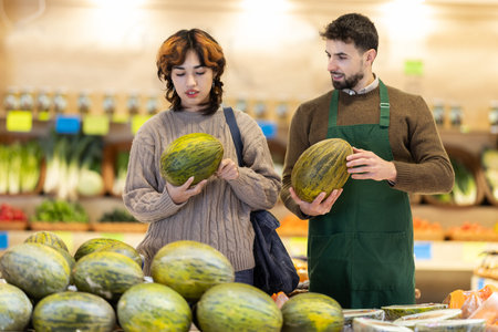 Young male seller offering melon to girl in grocery marketの写真素材