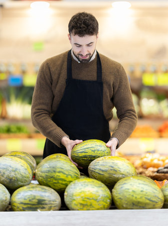 Young man seller puts melon in storeの写真素材
