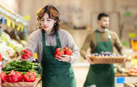 Young woman seller puts peppers in store