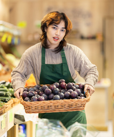 Young woman seller puts plums in storeの写真素材
