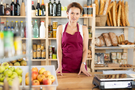Portrait of positive female salesperson behind supermarket counter. Interior of grocery supermarketの写真素材
