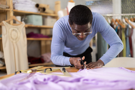 African man seamstress cuts fabric on cutting tableの写真素材