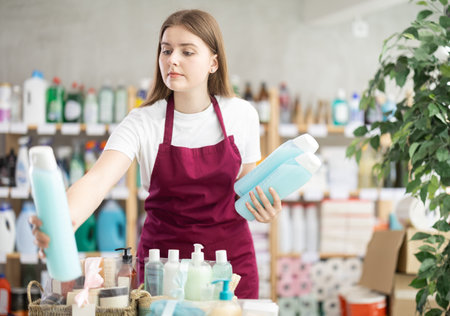 Sales girl places shampoo and shower gel on the shelves of supermarketの写真素材