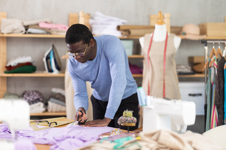 African man seamstress cuts fabric on cutting tableの写真素材