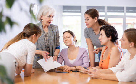 Women discuss documents sitting at table in office