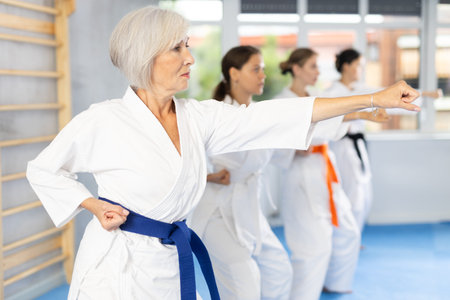 Elderly woman in white kimono performing kata routines at karate trainingの写真素材