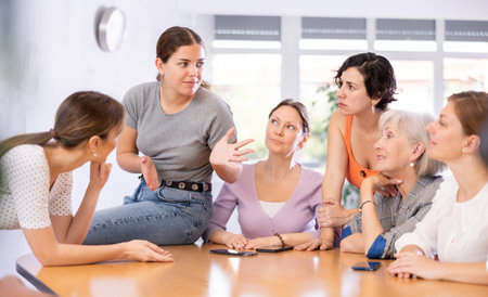 young girl student sits on table near friends and promotes version of solution of educational taskの写真素材