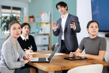 Interested office workers sitting at table discussing ideas and watching presentation during...