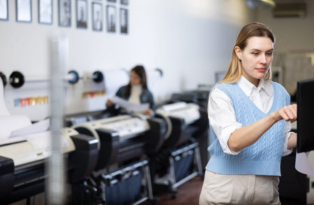 Female employee of the printing house adjusts the plotter using computer