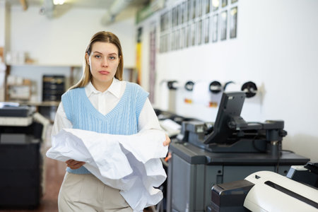 Portrait of a female employee of printing house with torn piece of paper in her hands