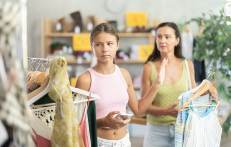 Teenage girl being capricious while shopping with mother in clothing storeの写真素材