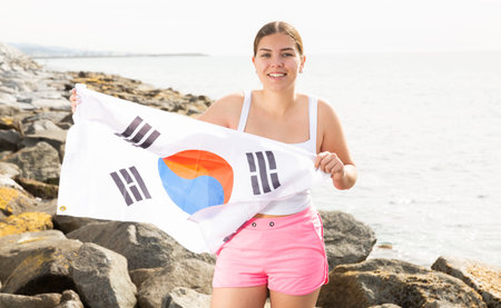 Happy girl waving the South Korea flag on the seashore on a sunny day. Rest on beach in South Koreaの写真素材