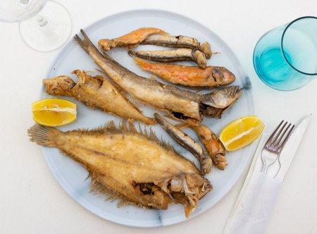 On white background, there is plate with fried fish of different varieties
