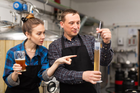 Couple of brewmasters using hydrometer to check alcoholic content in beerの写真素材