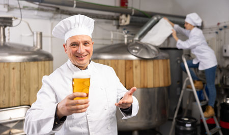 Cheerful man brewer presenting glass of beer
