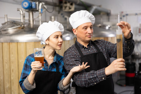 Couple of brewmasters using hydrometer to check alcoholic content in beer