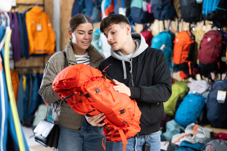 Young married couple in winter clothes chooses a durable backpack for a winter hike in tourist...