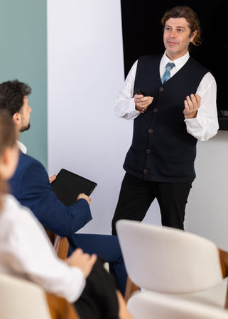 Male lecturer communicates and addressed to attendees, controls projector using remote controlの写真素材