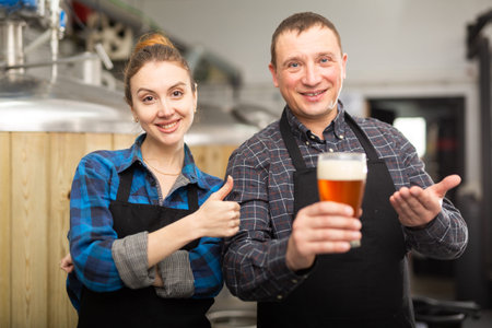 Smiling man and woman brewers presenting new beer in beer factory
