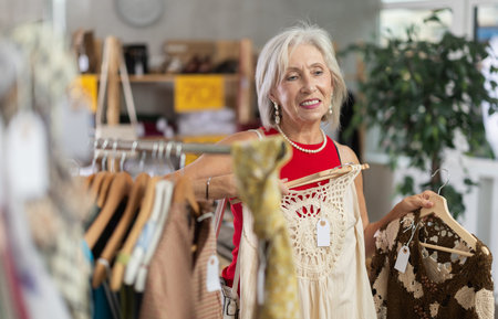 Positive mature woman choosing something for summer in clothing store