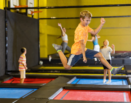 Full length of excited casual schoolchild boy having great time while jumping high on colorful...
