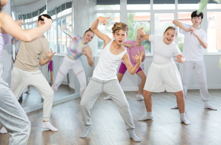 Male boy student repeats movements of unrecognizable teacher during group modern dance class.