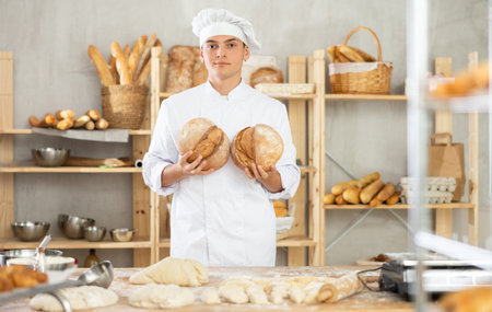 Bakery male employee holds ready made bread of bread in hands