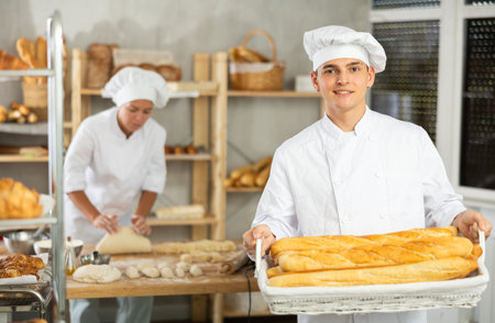 Young man is standing in kitchen with basket of finished products baguettes