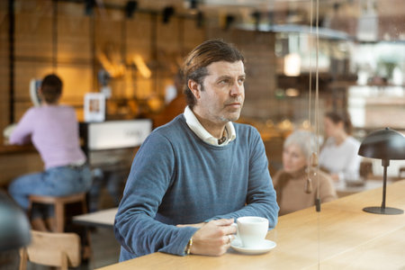 Thoughtful man drinking coffee at table in cozy cafe