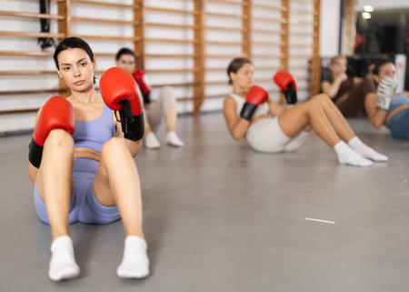 Young girl doing abdominal exercise with boxing gloves in group