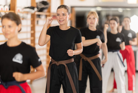 Positive young woman practicing kata standing in row with others