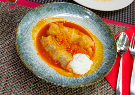 Homemade cabbage rolls in leaves of cabbage at plate with sour cream