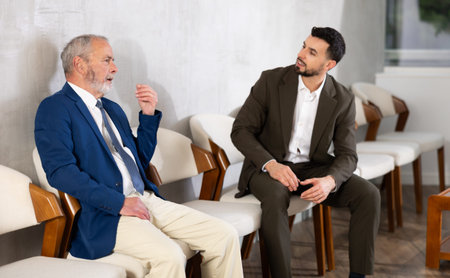 Young and elderly men talking while waiting in job interview queue
