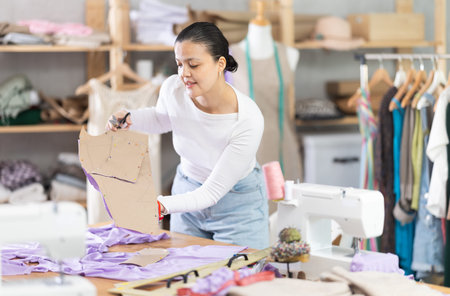 Experienced young asian girl fashion designer working working as cutter, using patterns and textiles...
