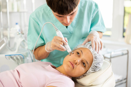 Young male cosmetologist doing microcurrent procedure to young woman
