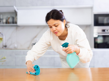 Positive young woman cleaning kitchen table at home