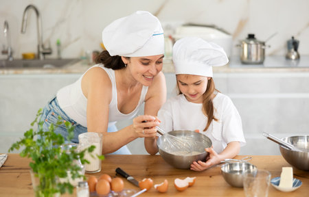 Happy mother and her daughter whisking ingredients in metal bowl in the kitchen
