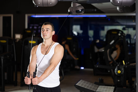 Active athlete young man during exercises on crossover exercise machine with loops and weighting